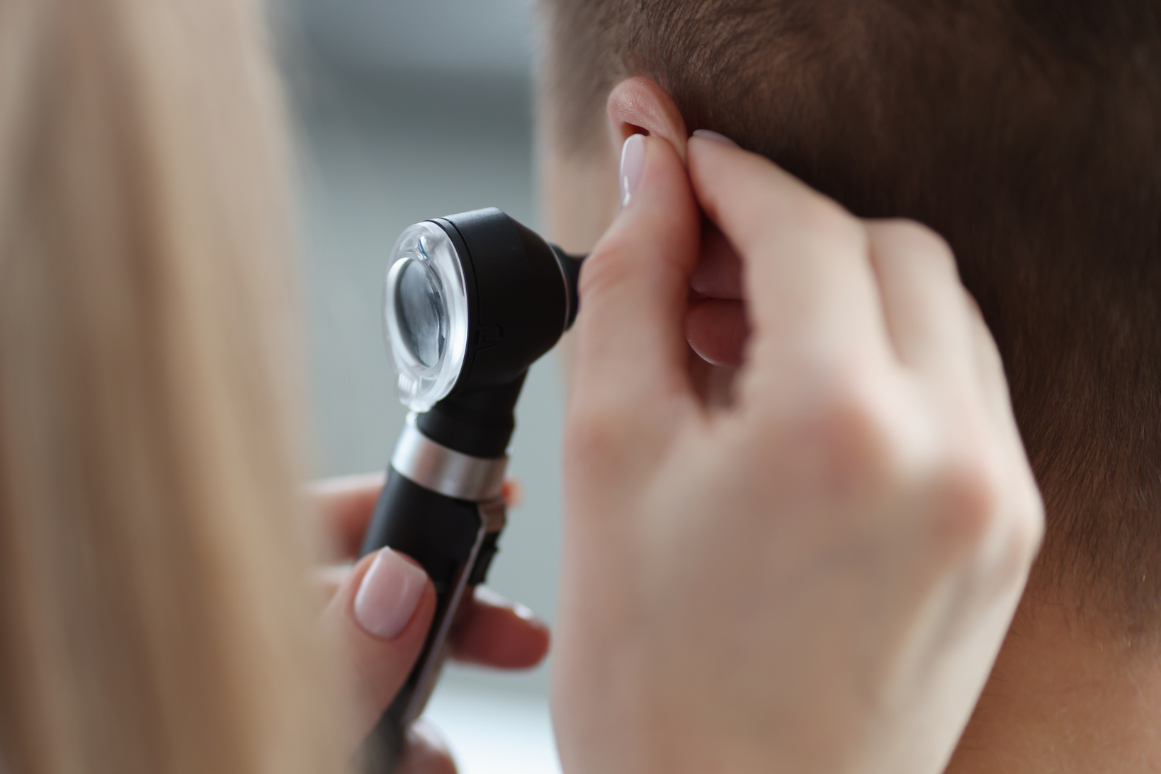 Otorhinolaryngologist Pulling Ear with His Hand and Looking at It with Otoscope Closeup